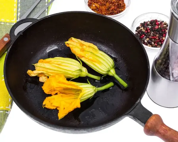 Fiori di zucca in padella, pronti per essere impanati e fritti. Accanto, spezie e sale per insaporire.
