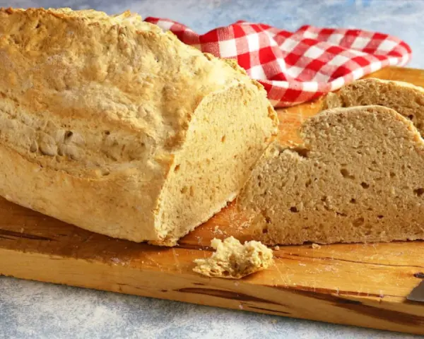 Pane casereccio con lievito istantaneo, tagliato su un tagliere di legno, con un tovagliolo a quadri rossi e bianchi.