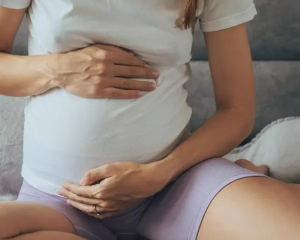 Brzuch kobiety w ciąży, z dłońmi delikatnie go obejmującymi.