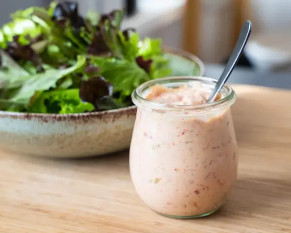 Ein Glas mit Thousand Island Dressing steht neben einer Schüssel Salat. Perfekt für den nächsten Salat!