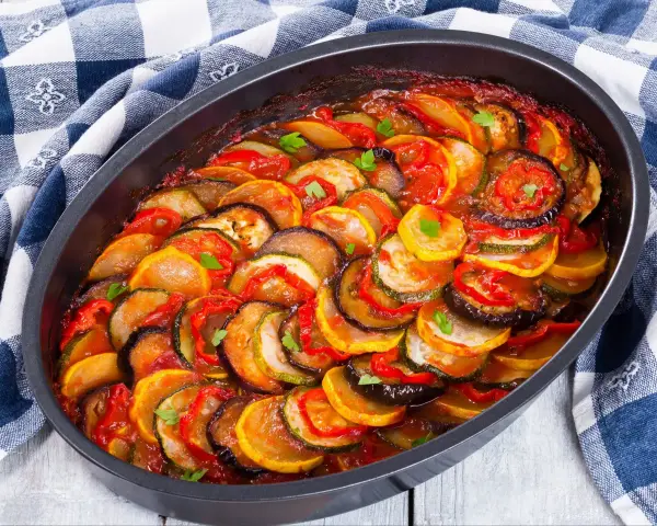 Gotowy ratatouille przepis w naczyniu żaroodpornym, z plasterkami cukinii, bakłażana i pomidorów, polany sosem.