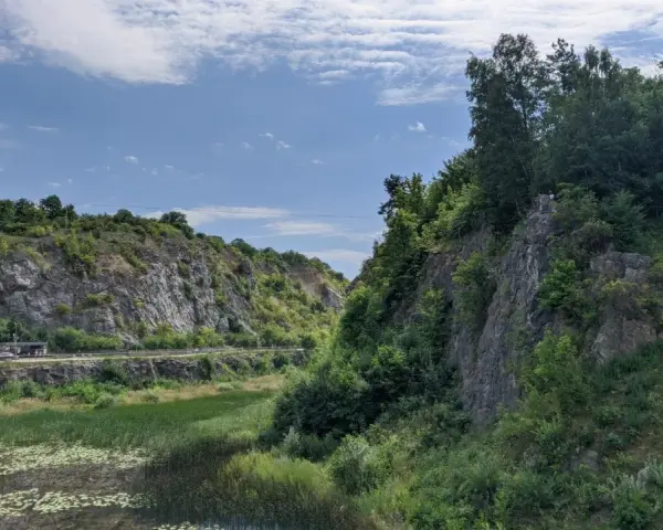 Kamieniołom z wodą i zielenią, skalne zbocza, niebo z chmurami.