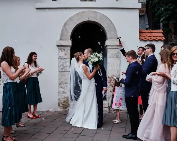 Para młoda całuje się przed kościołem, goście sypią bańki mydlane. To piękny ślub jednostronny, pełen radości i miłości.