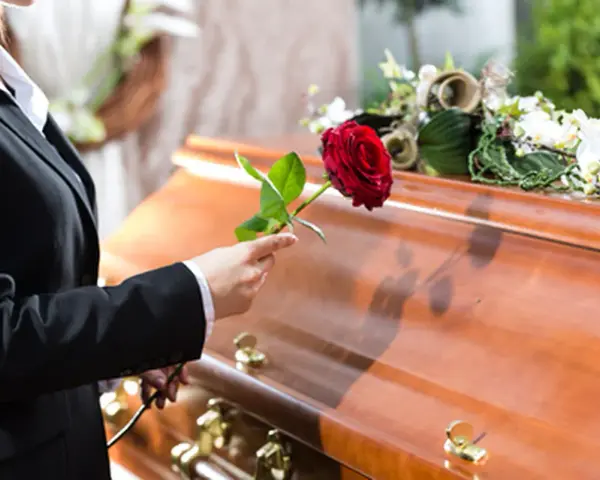 Eine Frau in Trauer legt eine rote Rose auf den Sarg. Sie muss die Beerdigung ihres getrennt lebenden Ehemanns bezahlen.
