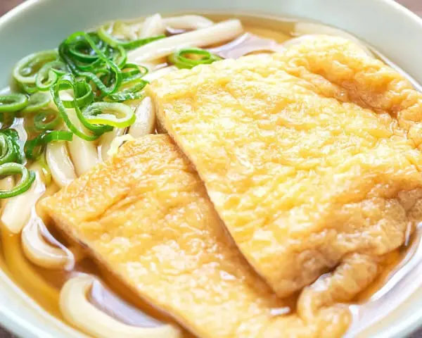 Pyszna zupa z makaronem udon z dwoma kawałkami smażonego tofu i zieloną cebulką.