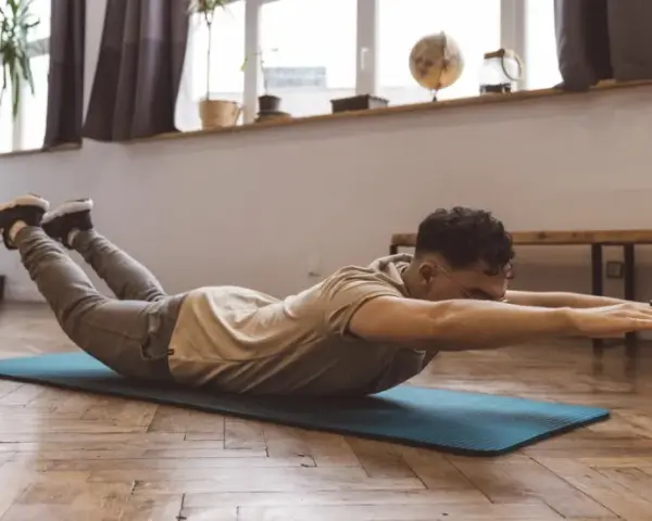 Homme faisant un exercice dos sur un tapis, bras tendus, jambes levées.