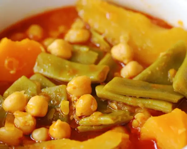 Un plato humeante de olla gitana, con garbanzos tiernos, judías verdes y trozos de calabaza en un rico caldo.