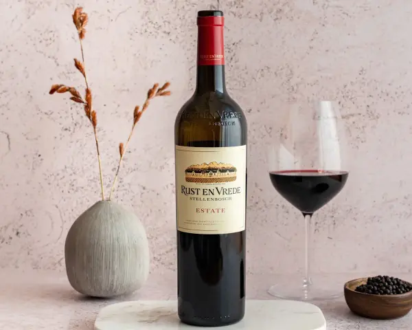 En flaska Rust en Vrede Estate vin, perfekt till oxfilé, står bredvid ett glas rött vin och en liten skål med pepparkorn.