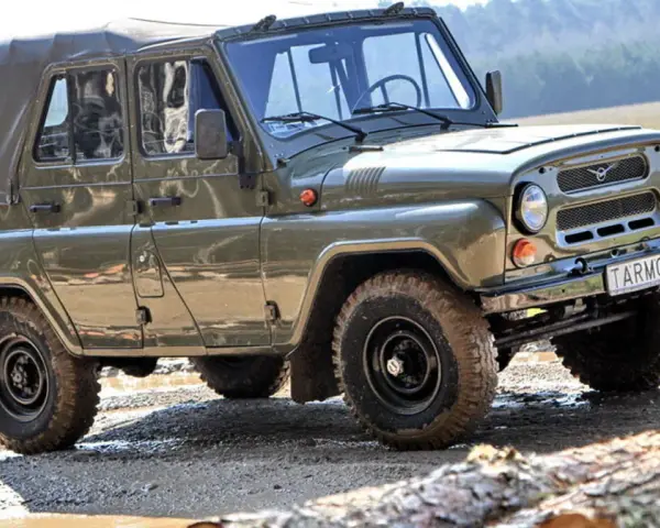 Zielony UAZ z plandeką, marka samochodu na u, pokonuje błotnisty teren.