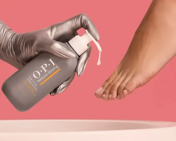Gloved hand dispenses OPI Nature Strong Pedi Soak, preparing to soak feet for a luxurious pedicure.