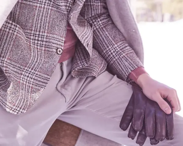 Un uomo indossa un elegante spezzato con giacca a quadri, maglione rosa e guanti in pelle marrone, pronto per l'inverno.