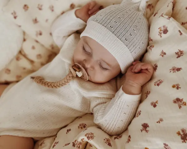 Śpiące dziecko w czapce i pajacyku z wełny merino. Czy wełna merino gryzie? Nie, jest miękka i delikatna dla skóry maluszka.