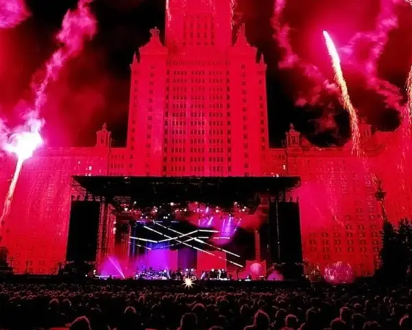 Ogromny budynek oświetlony na czerwono, fajerwerki i scena koncertowa. Tłum ludzi czeka na największy koncert na świecie.