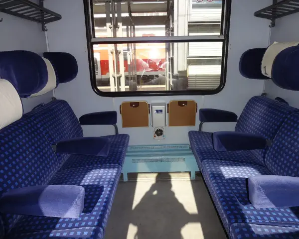 Wnętrze wagonu z niebieskimi siedzeniami w kratkę. Różne rodzaje wagonów oferują komfort podróży.