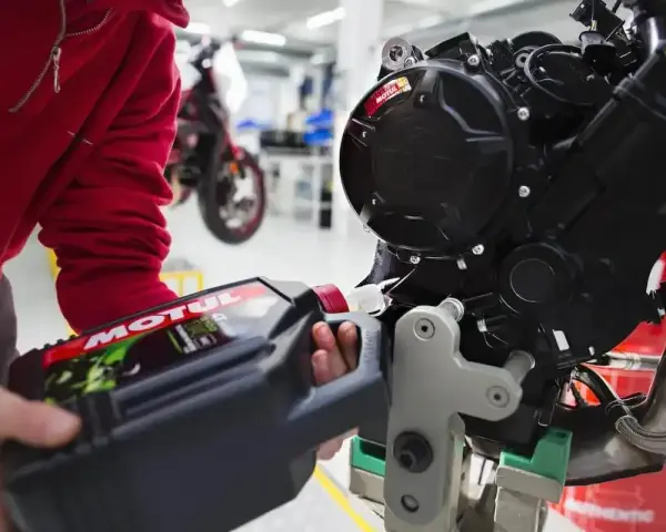 Osoba w czerwonej bluzie nalewa olej do silnika motocykla. Różne typy silników wymagają odpowiedniego smarowania.