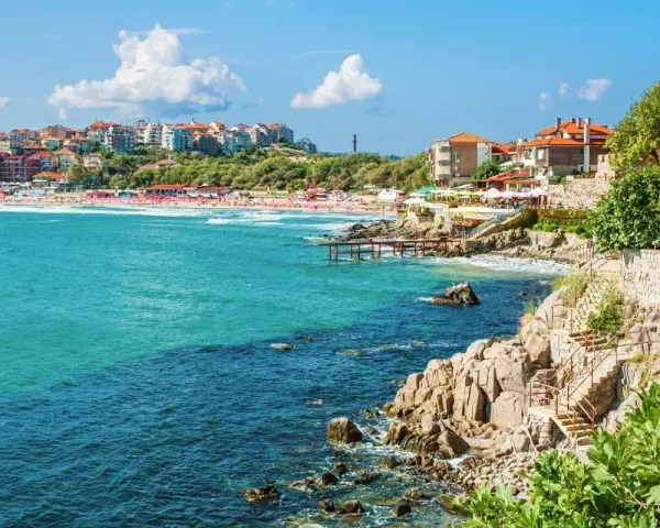 Widok na bułgarskie wybrzeże z kamienistymi klifami, plażą i zabudowaniami. Czy w Bułgarii są palmy? Tak, w niektórych miejscach można je spotkać.