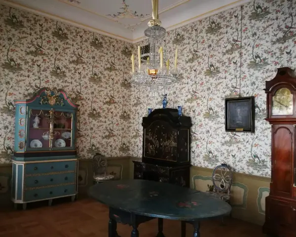 Wnętrze Uphagen House: zabytkowy zegar, szafka, stół i tapeta z ptakami.