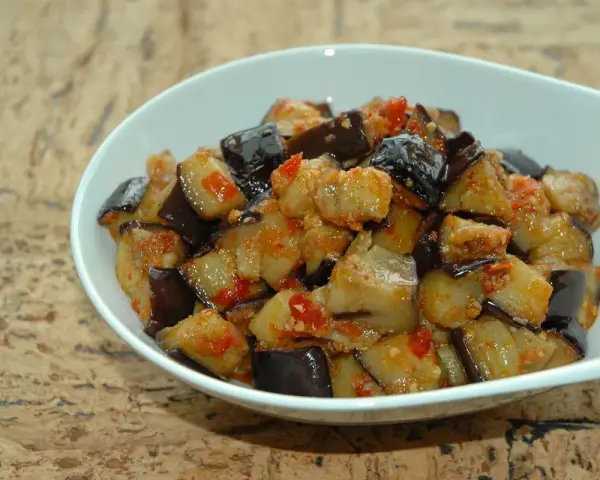 Melanzane al microonde, tagliate a cubetti e condite con pomodoro e spezie, servite in una ciotola bianca.