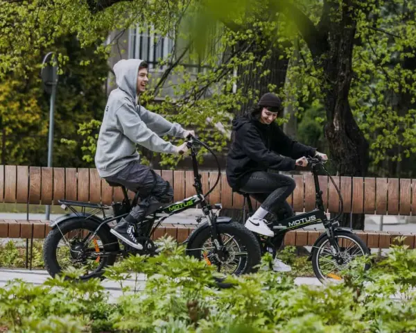 Dwaj młodzi ludzie cieszą się jazdą na rowerach elektrycznych. Dofinansowanie do roweru elektrycznego sprawia, że ekologiczny transport jest dostępny dla każdego.