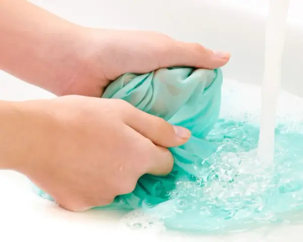Hände waschen ein türkises Tuch im Waschbecken, um Fettflecken zu entfernen. Wasser sprudelt und schäumt.