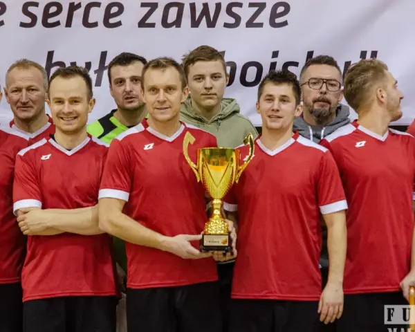 Drużyna w czerwonych koszulkach świętuje zwycięstwo z pucharem. W centrum stoi Andrzej Zaborowski, dumny z sukcesu.