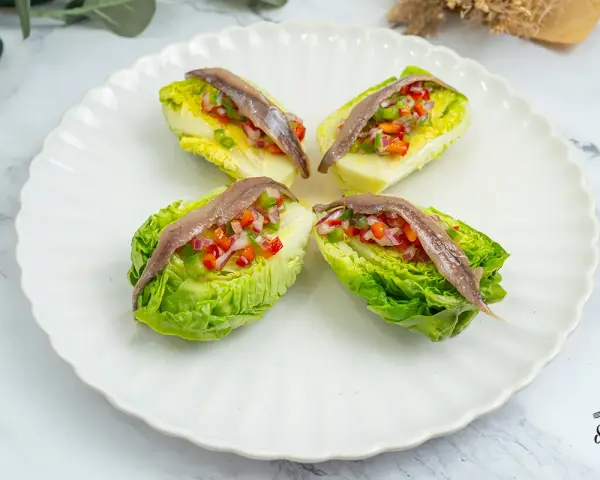 Cuatro cogollos de Tudela rellenos de pimientos y cebolla, coronados con anchoas. Frescura y sabor en cada bocado.