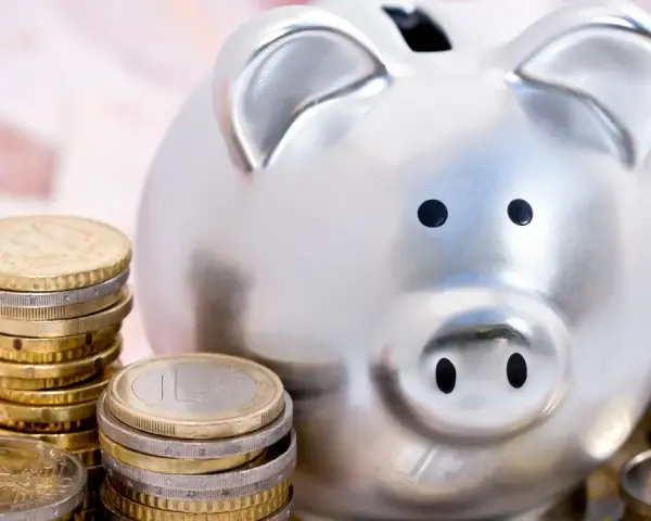 Hucha plateada rodeada de pilas de monedas de euro, simbolizando las ventajas del euro para el ahorro.