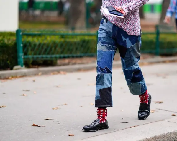 Uomo con jeans patchwork e mocassini neri, calzini rossi a fantasia.