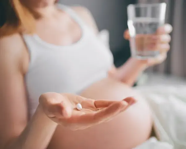 Kobieta w ciąży trzyma tabletkę i szklankę wody. Dba o siebie, przyjmując rutinoscorbin w ciąży.