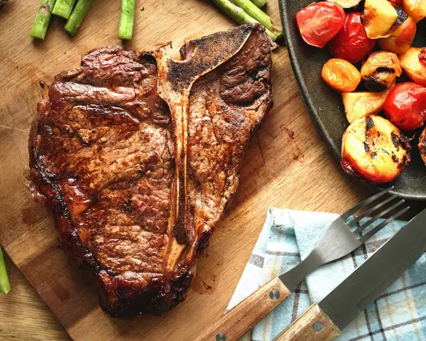 Un succulent côte de bœuf grillé, accompagné d'asperges et de tomates rôties, prêt à être dégusté.