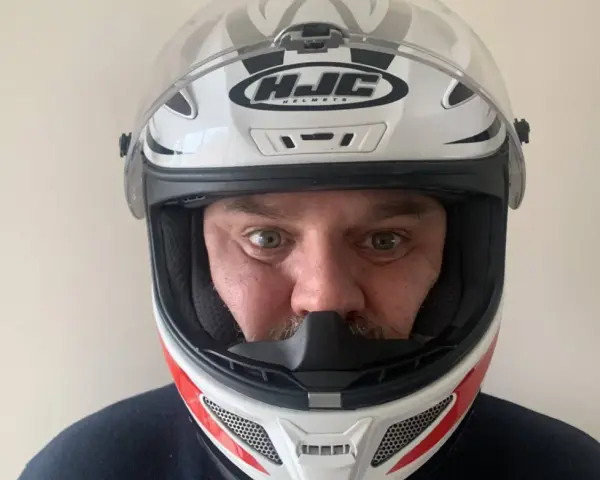 Hombre con casco HJC blanco y rojo, listo para elegir su equipo de moto.
