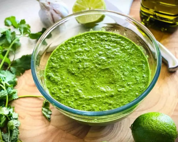Frisch zubereitetes mojo verde in einer Glasschüssel, umgeben von Koriander, Knoblauch, Limetten und Olivenöl.