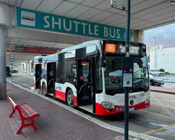 Autobus wahadłowy z otwartymi drzwiami na przystanku lotniskowym, z napisem "SHUTTLE BUS".