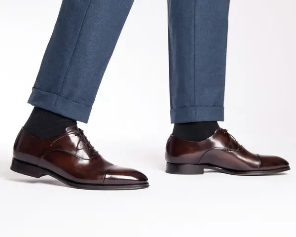 Eleganza senza tempo: un uomo indossa pantaloni blu e scarpe oxford non brogue marroni lucide, perfette per ogni occasione formale.