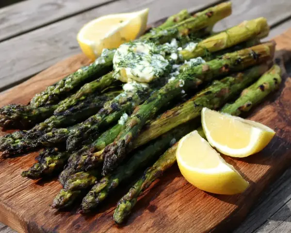 Grilla sparris med smör och dill, serverad med citronklyftor på en träskärbräda. Perfekt sommarbuffé!