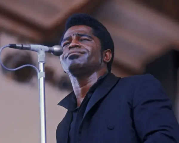 Le chanteur funk français James Brown, en sueur, chante passionnément dans un microphone.