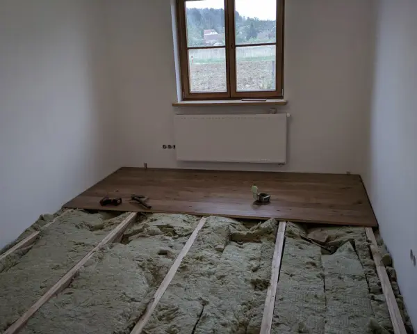 Podłoga na legarach na poddaszu, w trakcie montażu drewnianych desek. Widoczna wełna mineralna izolacyjna.
