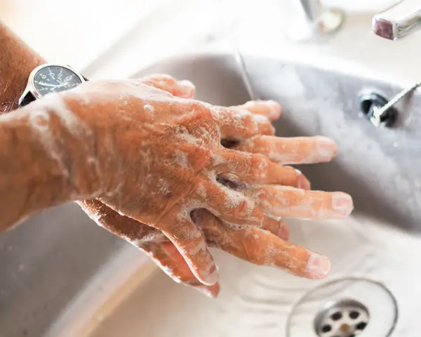 Manos con jabón bajo un chorro de agua en un lavabo.