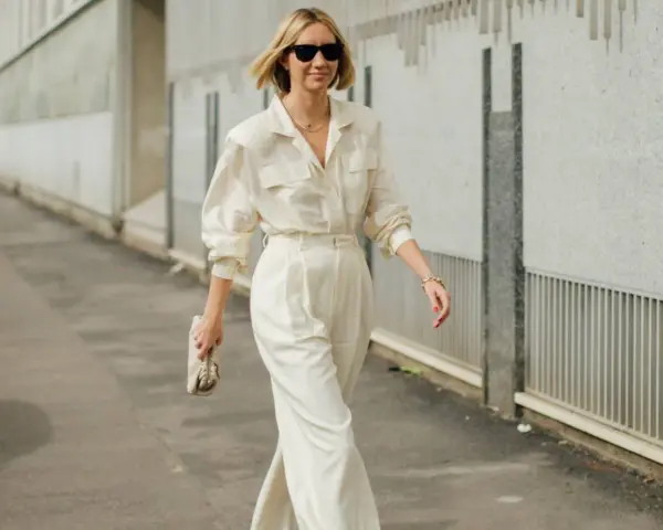 Mujer con un elegante outfit oficina verano: pantalón ancho blanco, camisa holgada y bolso de mano.