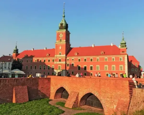 Słoneczny dzień na placu zamkowym w Warszawie. Ludzie odpoczywają na murze przy Zamku Królewskim.