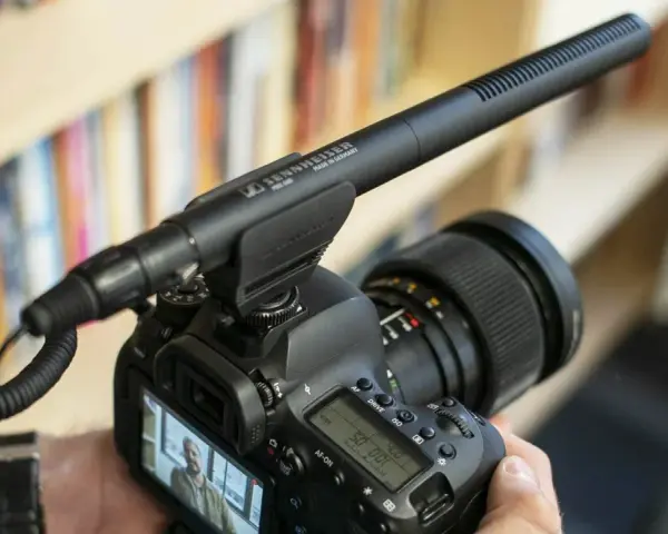 Kamera z mikrofonem kierunkowym Sennheiser MKE 600 na gorącej stopce. Tło to półka z książkami.