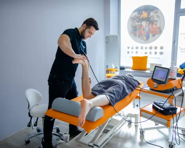 Fizjoterapeuta wykonuje zabieg naświetlania kręgosłupa pacjentowi leżącemu na kozetce.