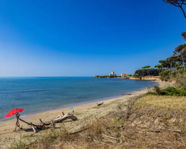 Torre Astura e la sua spiaggia, con un ombrellone rosso e una persona che si rilassa su un tronco.