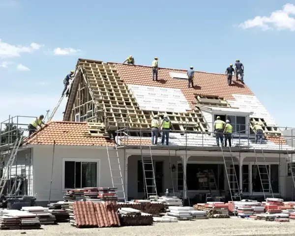 Ekipa budowlana pracuje nad remontem dachu domu. Widać rusztowania, drabiny i materiały budowlane.