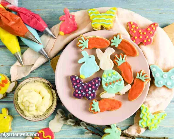 Bunte Osterkekse in Hasen-, Karotten- und Schmetterlingsform, bereit für ein einfaches Osterkekse Rezept. Spritzbeutel mit Zuckerguss liegen bereit.