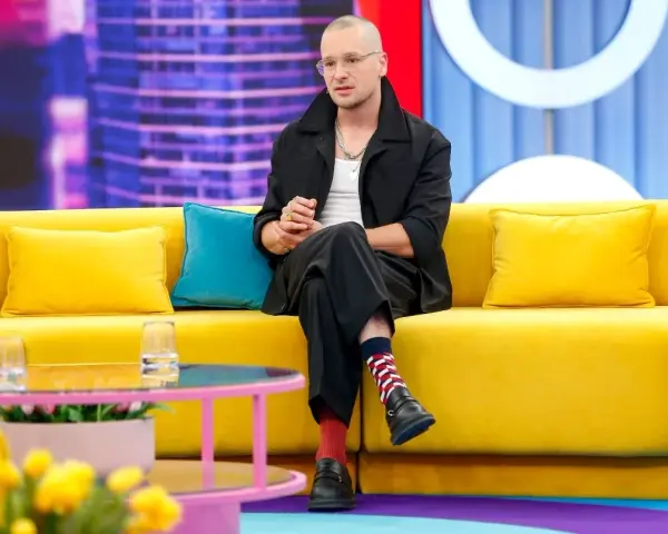 Krzysztof Zalewski w czarnym garniturze siedzi na żółtej kanapie, jakby przygotowywał się do nagrania jednego z jego filmów.