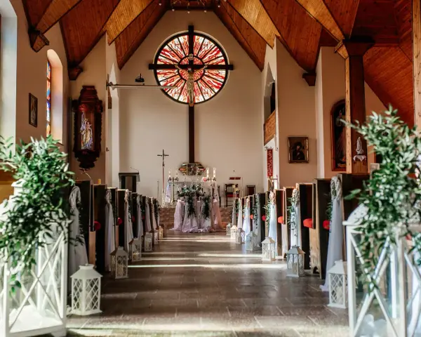 Piękne wejście do kościoła ślubnego, ozdobione zielenią i lampionami.