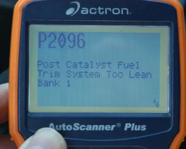 An orange and blue Actron AutoScanner Plus displays error code P2096: Post Catalyst Fuel Trim System Too Lean Bank 1.