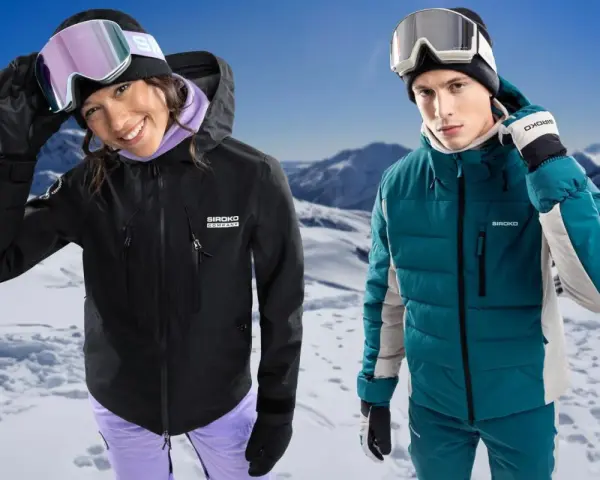 Coppia con abbigliamento da sci, giacche hardshell e maschere da neve, su sfondo montuoso innevato.