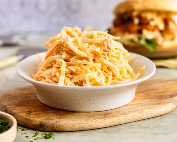 Schüssel mit cremigem Krautsalat, perfekt für ein **Rezept Coleslaw original**. Im Hintergrund ein Burger.